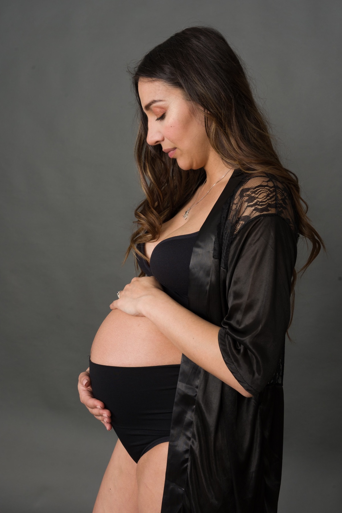 Mujer embarazada vestida de negro sobre fondo gris.