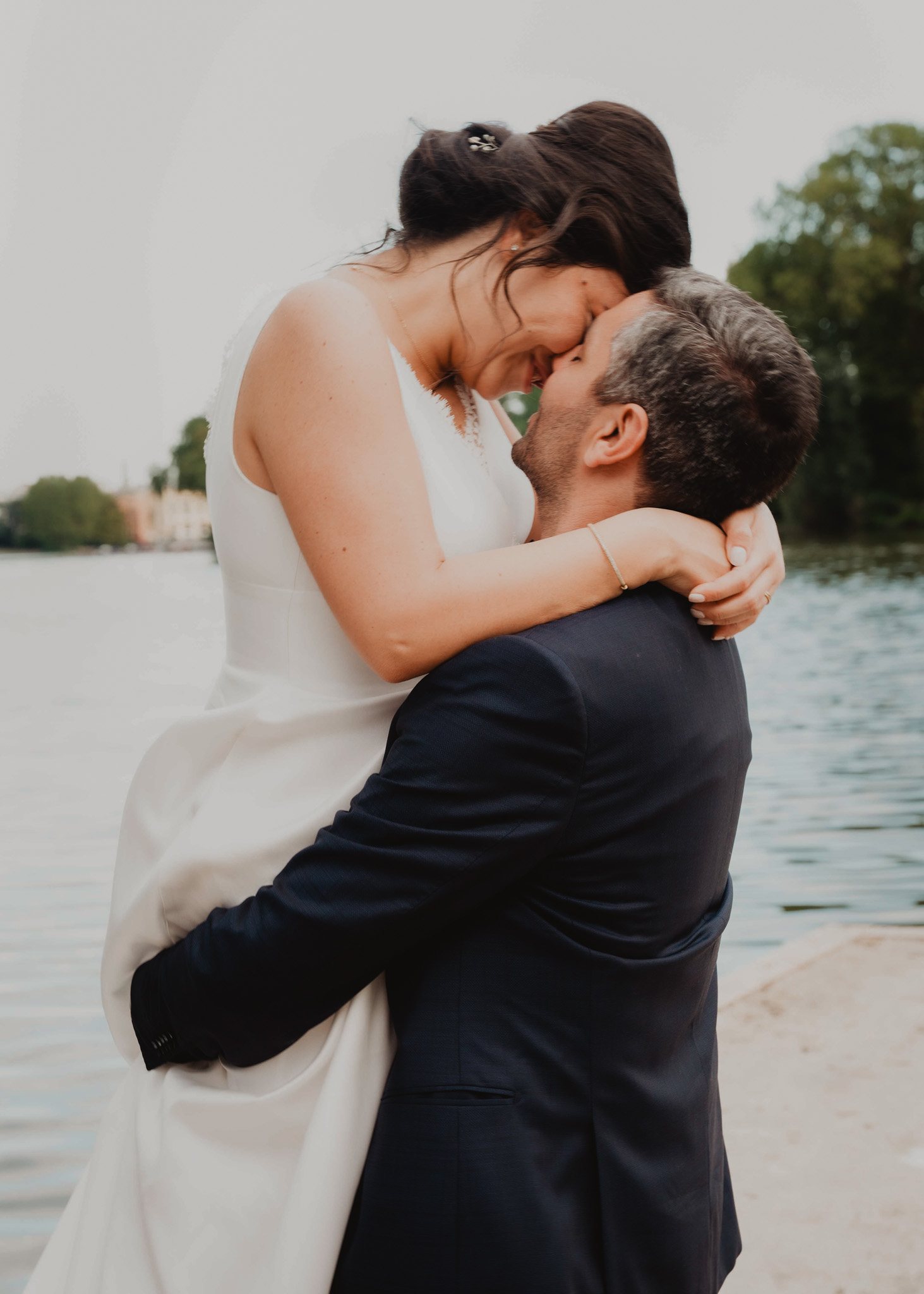 Un couple de jeunes mariés s'enlace près de l'eau.
