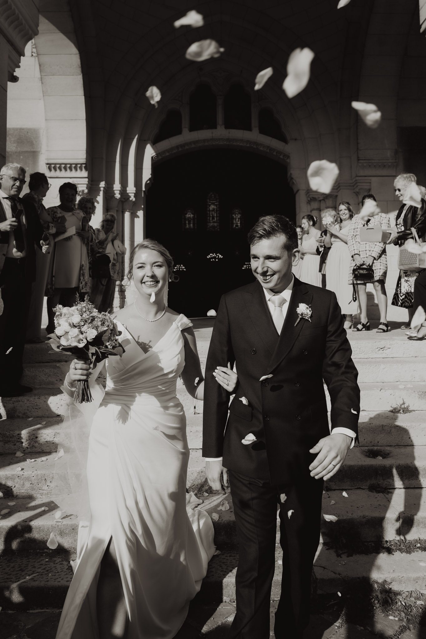 Un couple sort de la cérémonie en souriant, en noir et blanc.