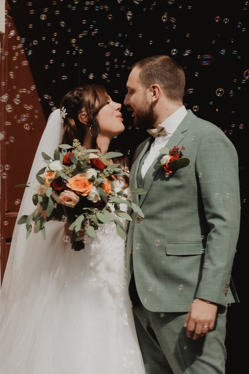 Un couple tient son bouquet devant un mur de pierre.