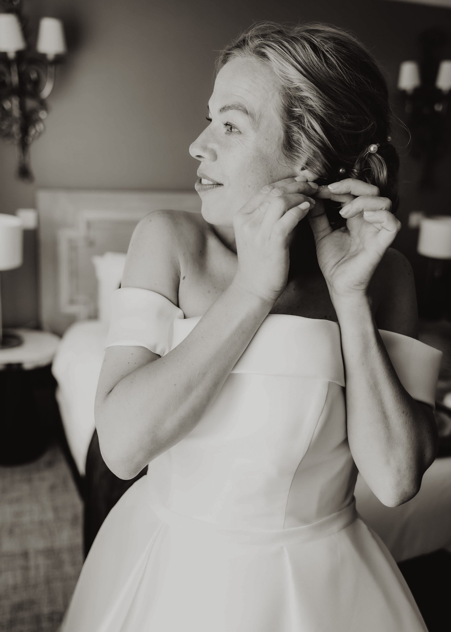 Une mariée met une boucle d'oreille pendant les préparatifs en noir et blanc.