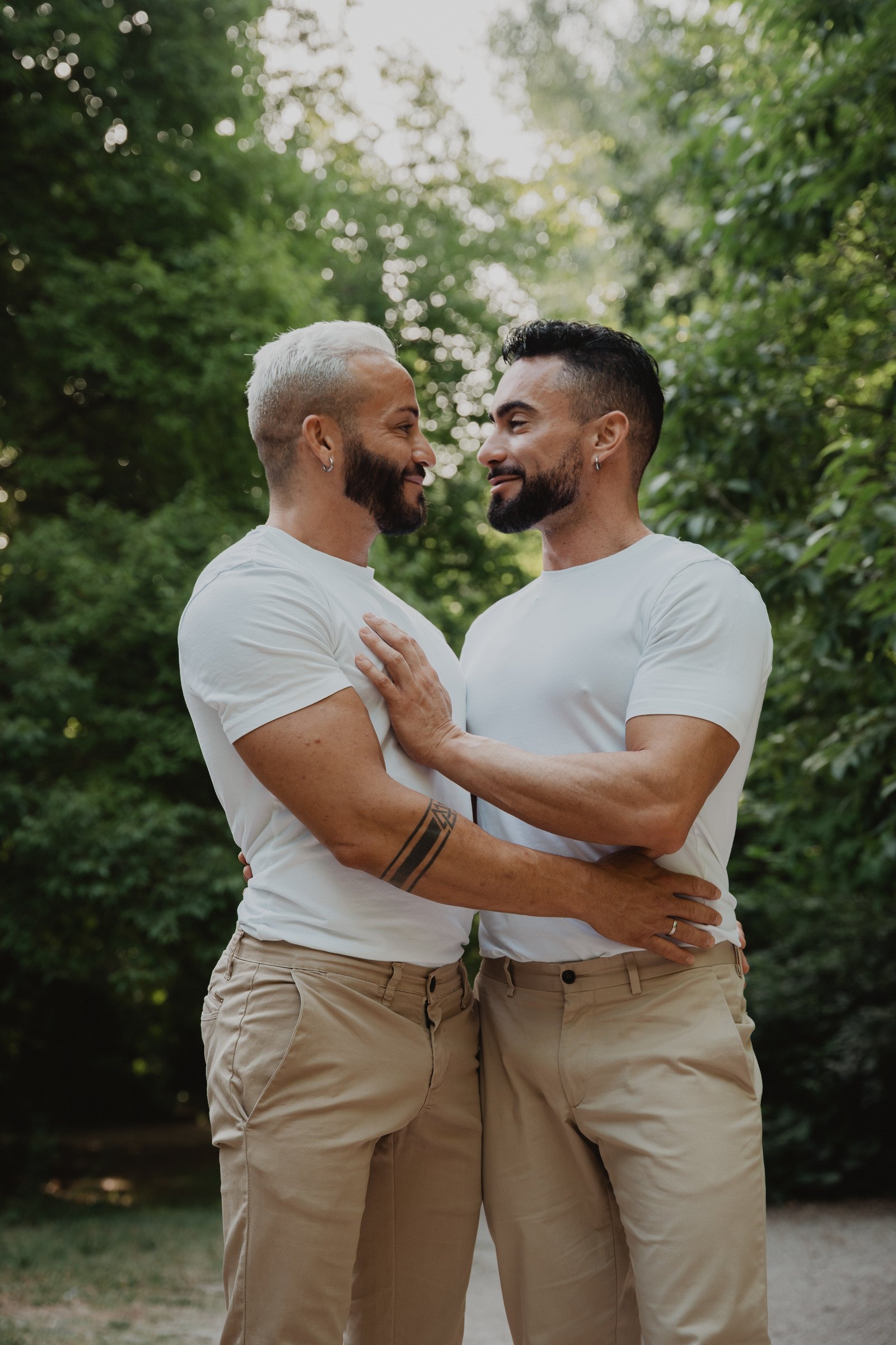 Deux hommes se regardent et sourient pendant une séance avant le mariage en plein air.