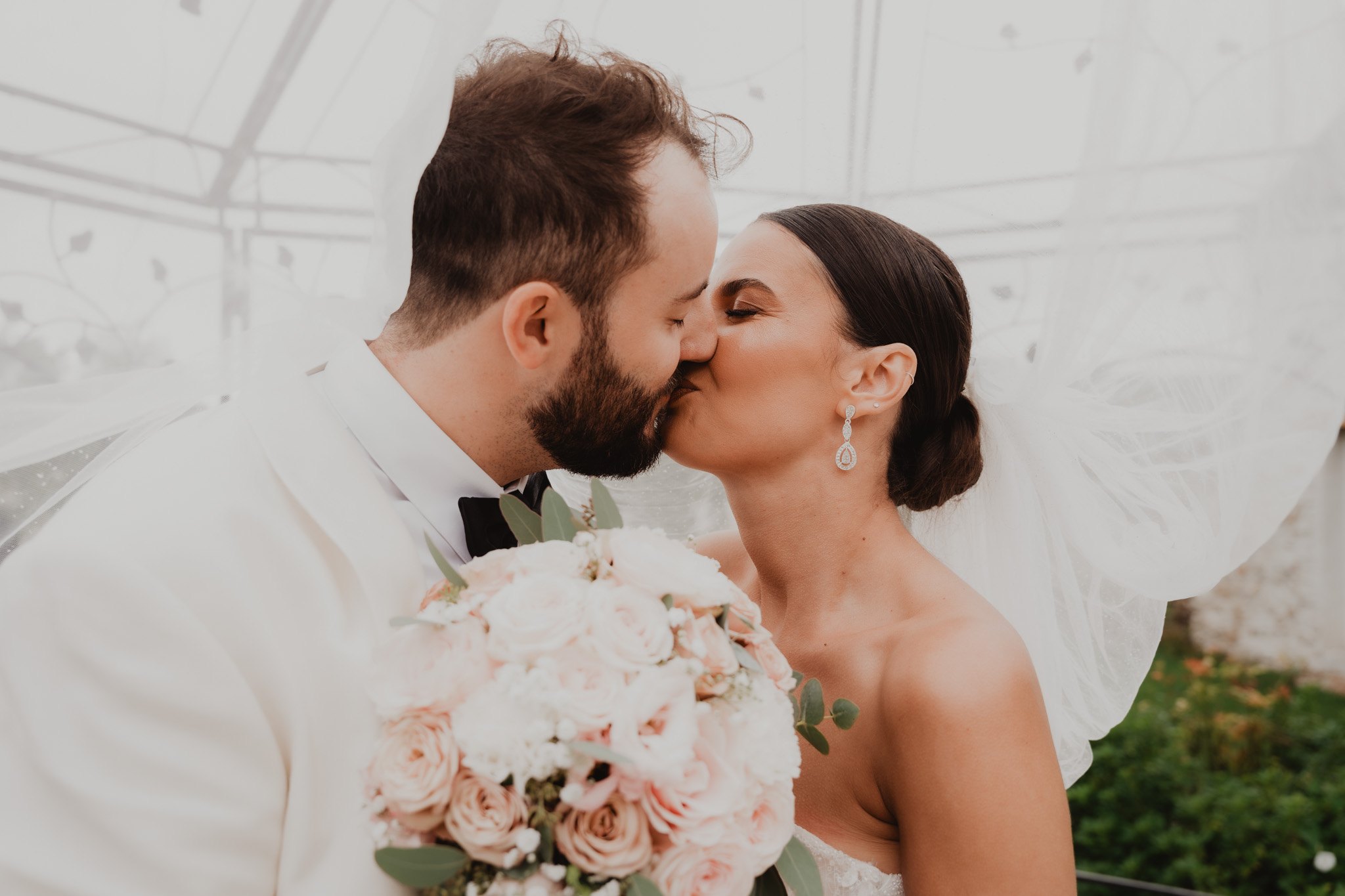Un couple s'embrasse derrière un bouquet de fleurs claires.