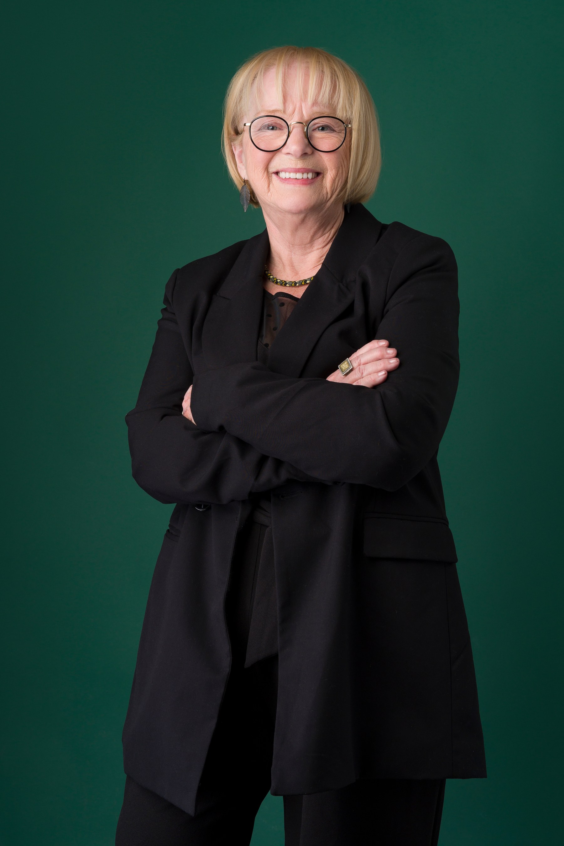 Retrato profesional de una mujer con chaqueta negra sobre fondo verde profundo.
