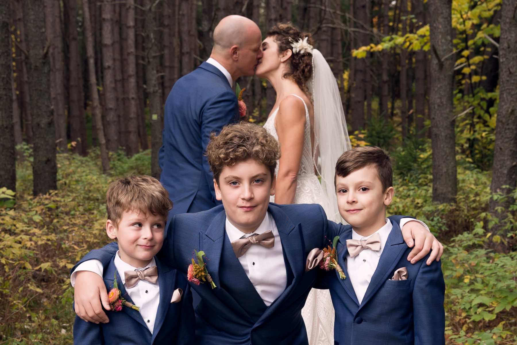 Nadia y Brendan se besan en el bosque con tres niños en primer plano.
