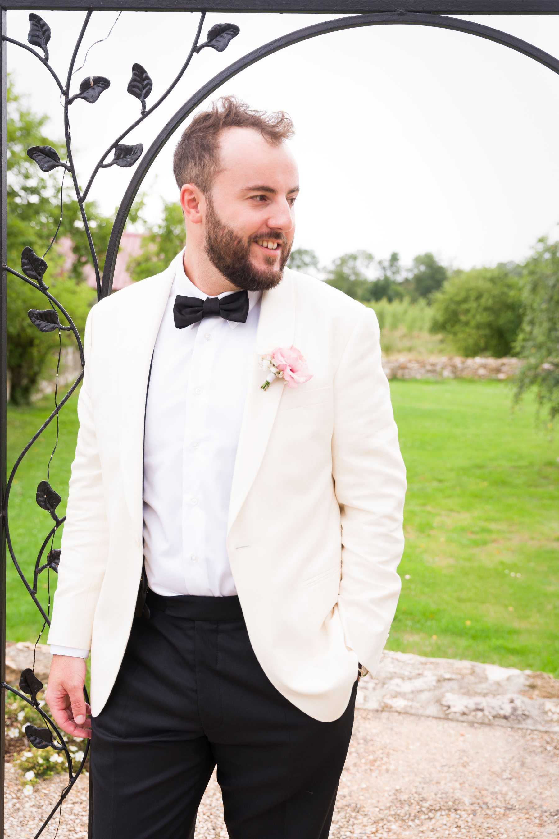 Florian posa con traje blanco junto a un arco de jardín.